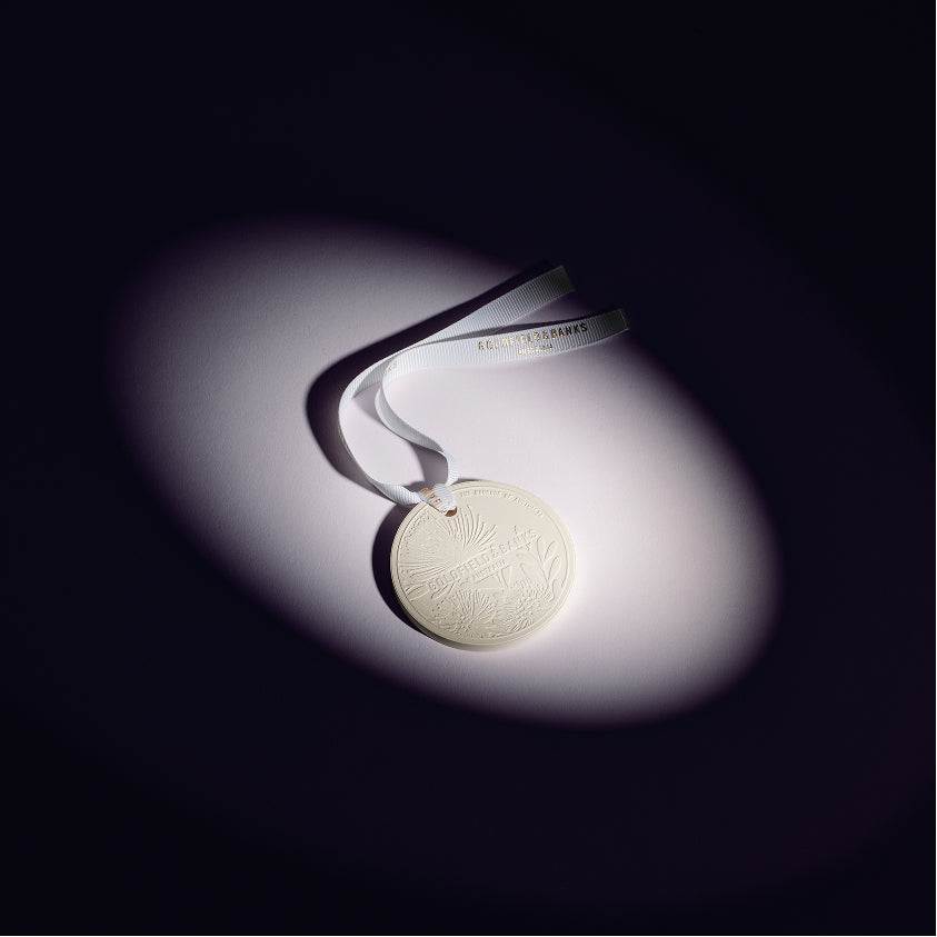 Mystic Bliss scented round ceramic ornament with white ribbon on dark background
