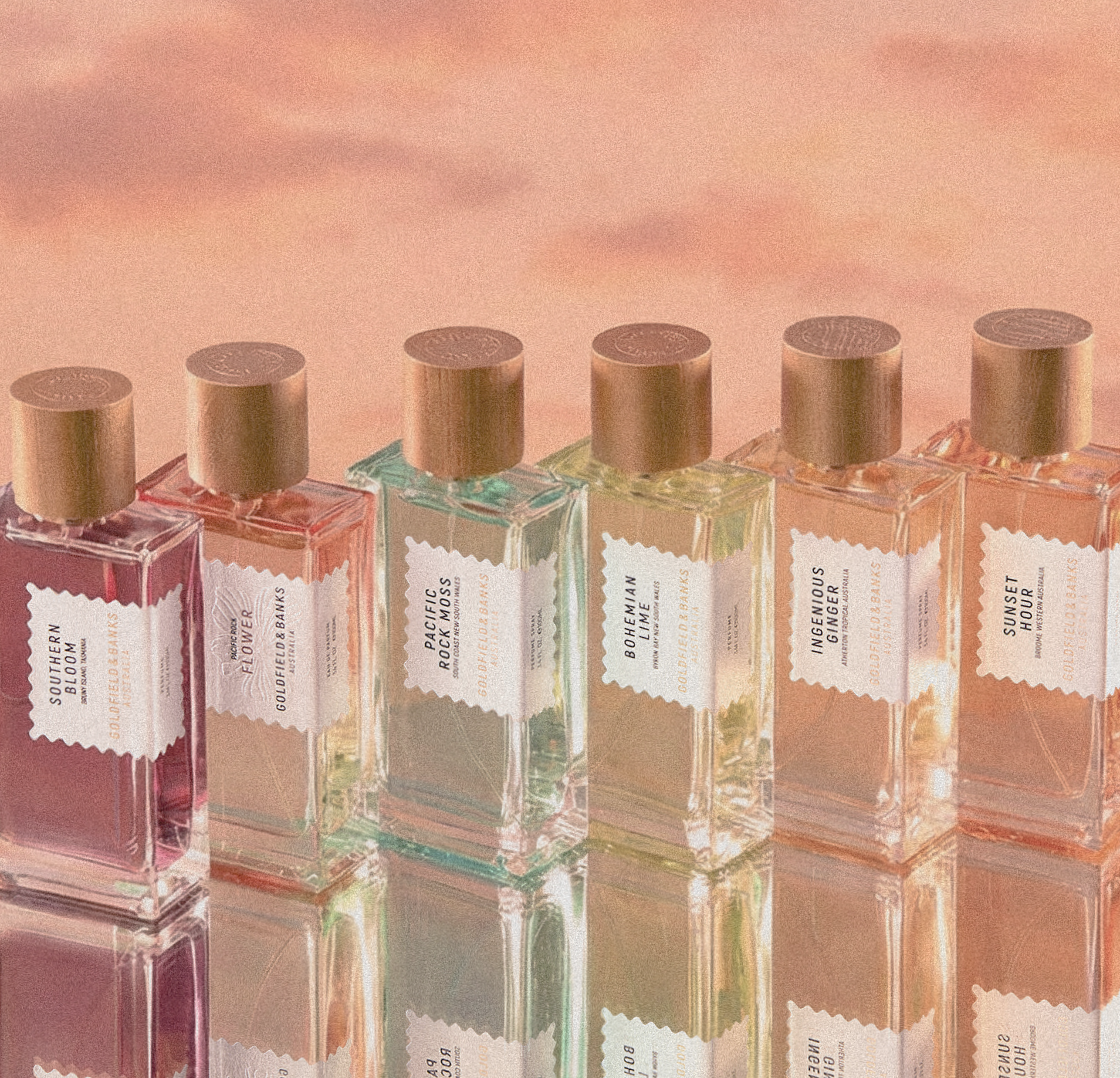 Goldfield & Banks luxury perfumes displayed in elegant glass bottles with gold caps, showcasing the Australian fragrance collection in pastel hues against a sunset background.
